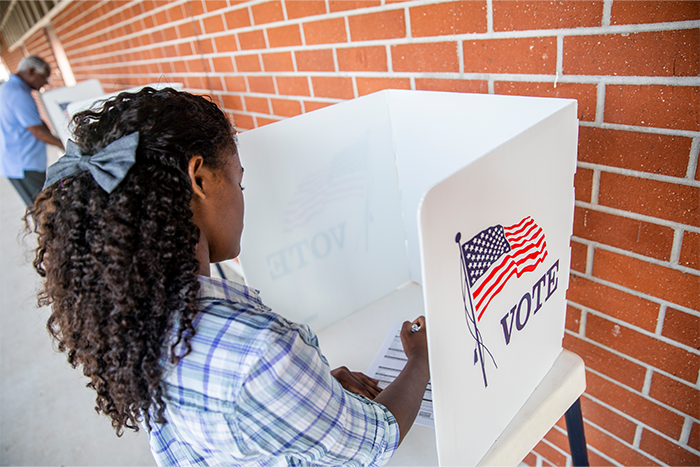 Person at a voting booth filling out a ballot in front of a brick wall