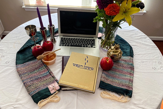laptop computer, prayerbook, tallis, candles, and flowers on a table