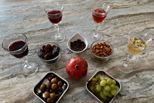 Elements of a Tu BiShvat seder on a marble countertop including wine grapes nuts and pomegranates