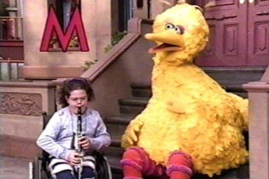 Disability activist Emily Ladau playing saxophone wiht Big Bird on Sesame Street