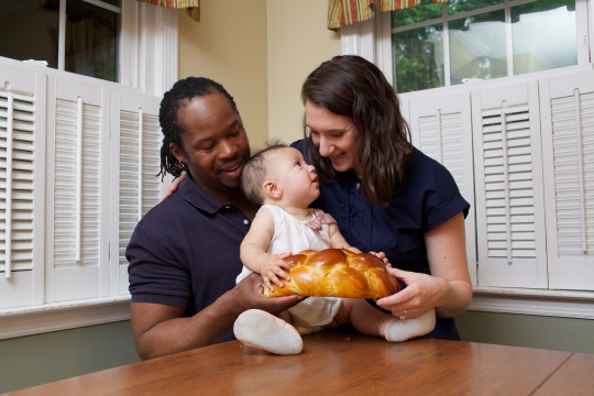 Parents holding their child on a table while the child holds a challah
