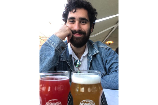 A person in a blue jean jacket sitting at a table in front of two glasses of beer