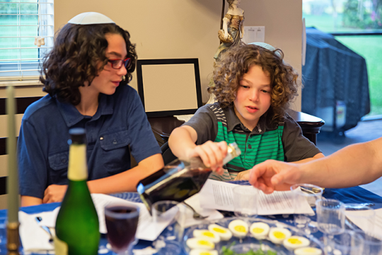 an image of two kids at a passover seder; one of them is pouring grape juice into a cup