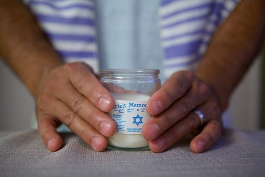 Photo of two hands holding a memorial candle, with white label and a blue star of david on it