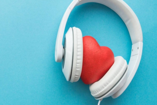 White headphones around a plastic heart against a bright blue background 
