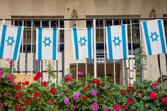 String of Israeli flags, wrought iron fence and blooming flowers
