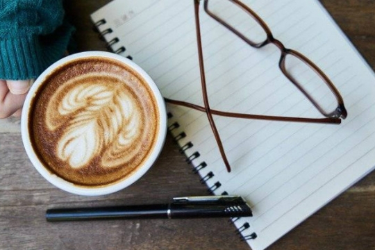 Womans hand holding a coffee cup next to a pen and a pad of paper